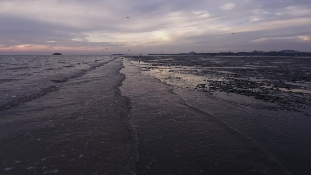 waves coming into the mudflat, track in shot, drone shot, sunset