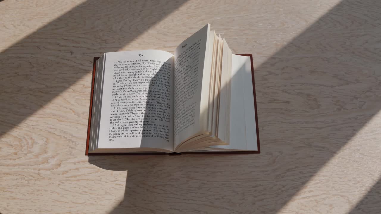 Aerial view of an open book on a wooden table, sunlight casting shadows, creating a serene