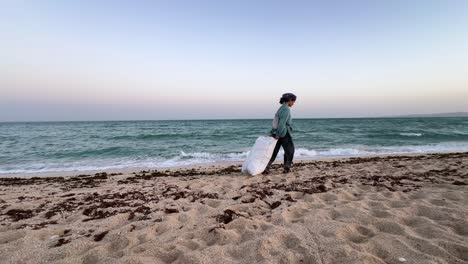 person walking along a beach carrying a bag