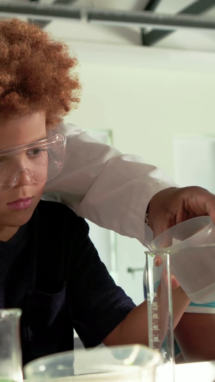 Vertical video: Lab-coated adult guiding two boys pouring green into cylinder in lab to measure