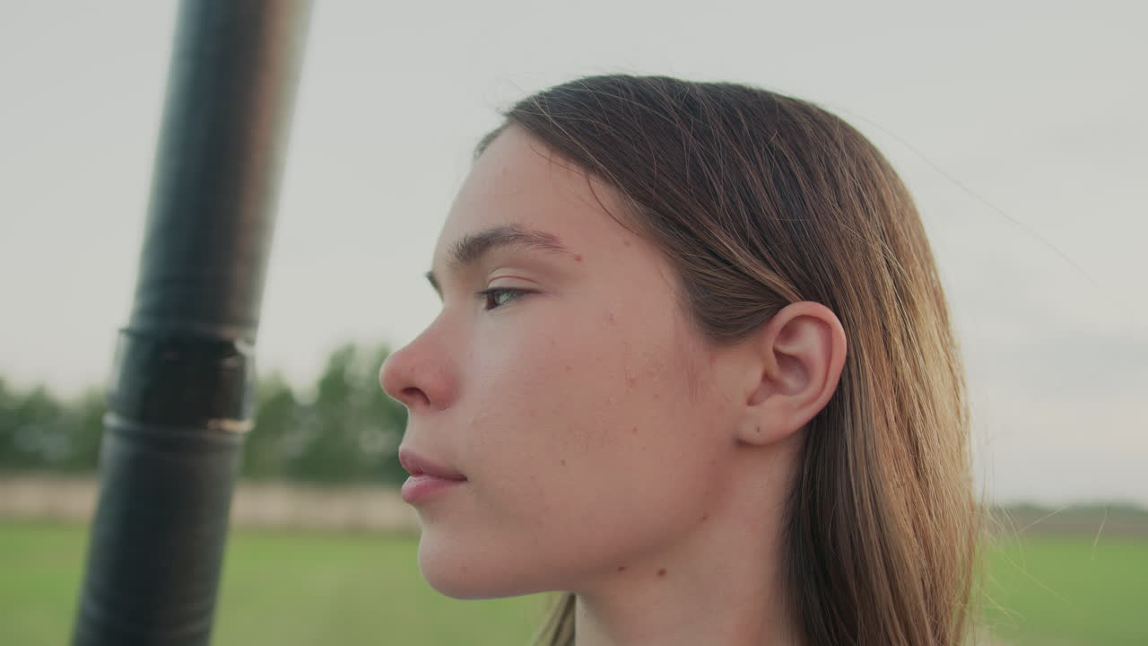 close up side profile of young lady with calm expression looking away during serene hot air balloon ride above farmland under soft sky as natural light highlights her features and contemplative mood