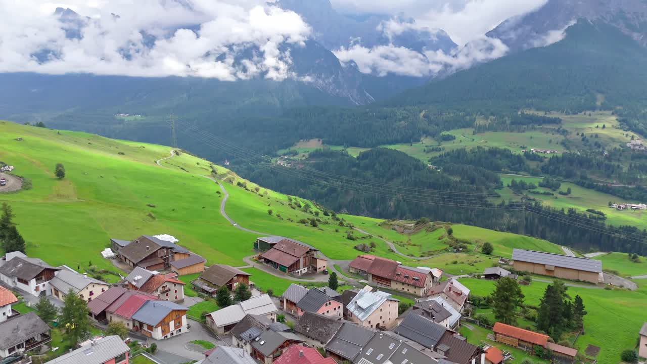 Peaceful idyllic Swiss village with houses, homes and apartments on hillside. Cloudy summer day in Switzerland. Aerial flyover shot