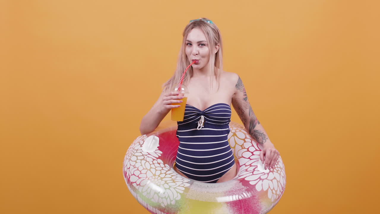 Woman in swimsuit with inflatable ring drinking juice