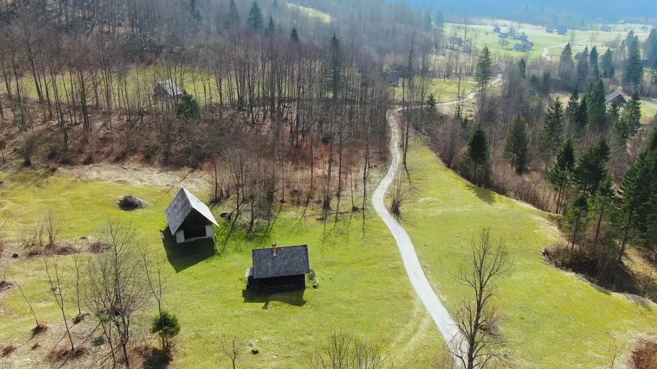 Medium wide aerial dolly in drone shot of mountain huts, roads and trees in Julian alps, bohinj, Triglav national park during the day