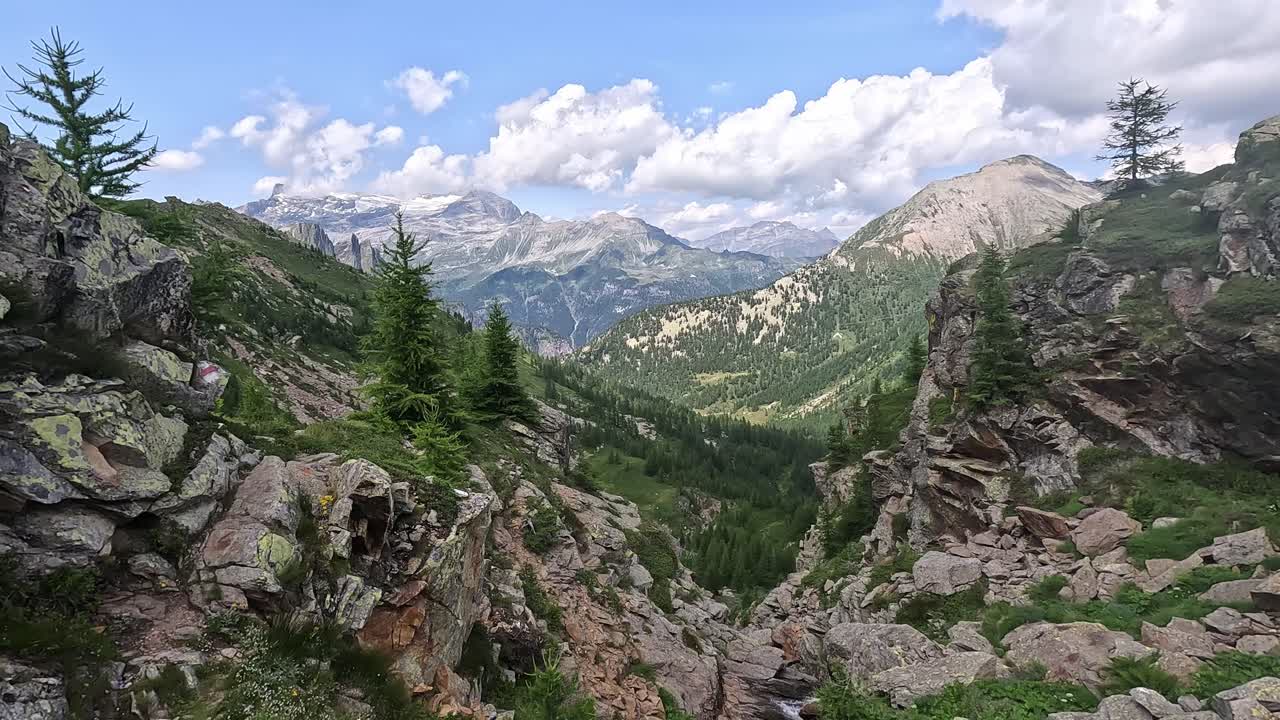 Ampia vista di una valle alpina con terreno roccioso, pini e cime innevate in lontananza nel Parco Naturale dell'Alpe Devero, Italia