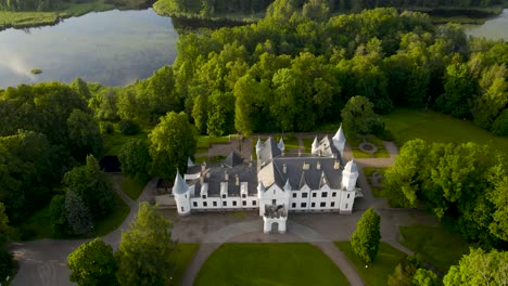 aerial drone footage descending and flying lower in front of a white colored mystical and fairytale like castle in alatskivi during a summer sunset with a large lake behind the castle with towers