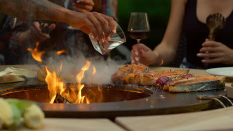 Hombre-Chef-Vertiendo-Aceite-En-La-Comida-Afuera.-Comida-De-Barbacoa-Casi-Terminada-Dorándose-Al-Aire-Libre.