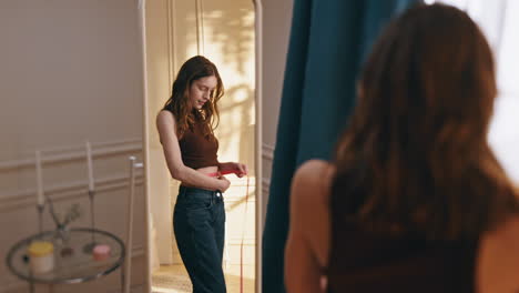 happy girl checking waist with measuring tape in mirror reflection at sunny home