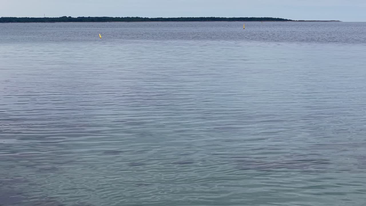 Drone footage captures a rocky shoreline in Denmark with calm blue sea, gentle waves, and a grassy hillside. The coastal scene highlights natural beauty and tranquility from above