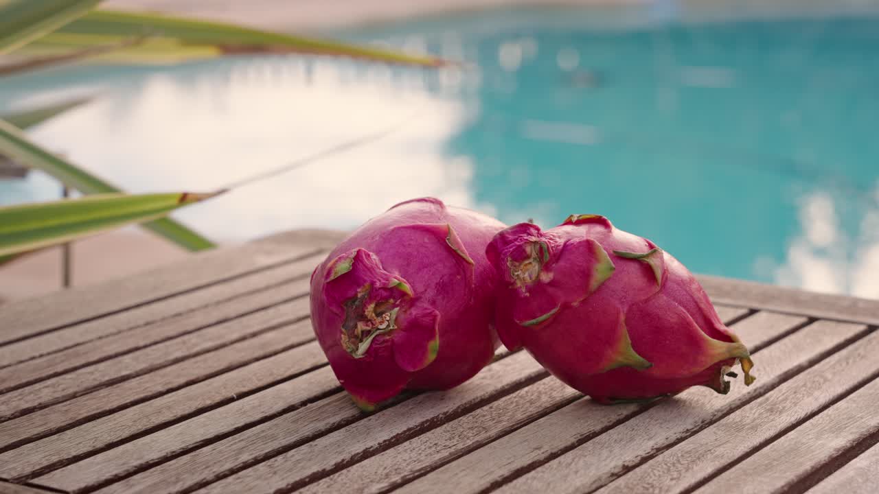 Dragon fruit on wooden table with swimming pool in the background at sunset - spinning camera
