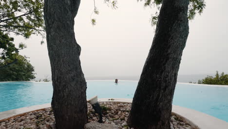 cinematic slomo shot of a girl in the pool between trees while it is raining outside, slow motion, philippines, asia