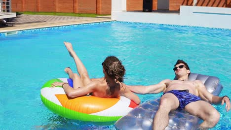 Young-attractive-people-swimming-on-inflatable-tubes-on-the-pool-party.-Pretty-women-and-men-having-a-pool-party.-Slowmotion-shot