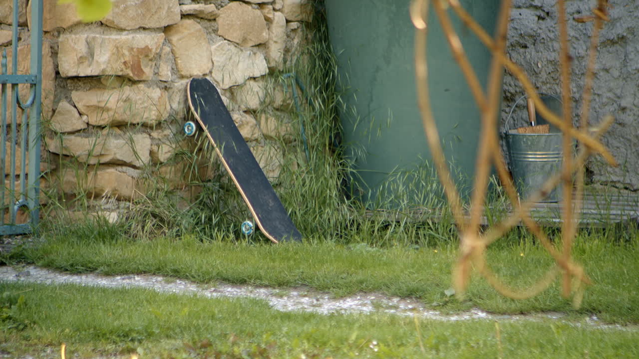 Unused skateboard leans against stone wall in quiet yard