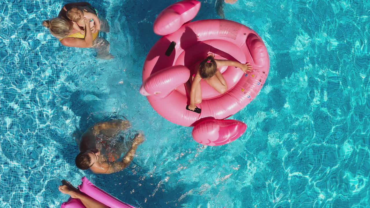 Overhead Drone Shot Of Multi-Generation Family With Inflatables On Summer Holiday In Swimming Pool