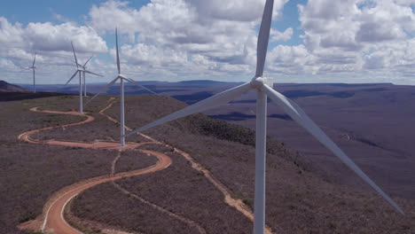 panoramic view of wind turbines rotating in sunny day. aerial panning showing lots of towers in a brown mountains background