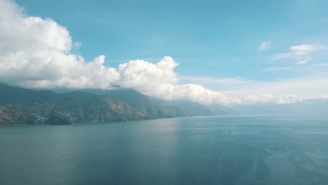 drone aerial perspective of blue lake atitlan during sunny day with clouds in the mountains in guatemala