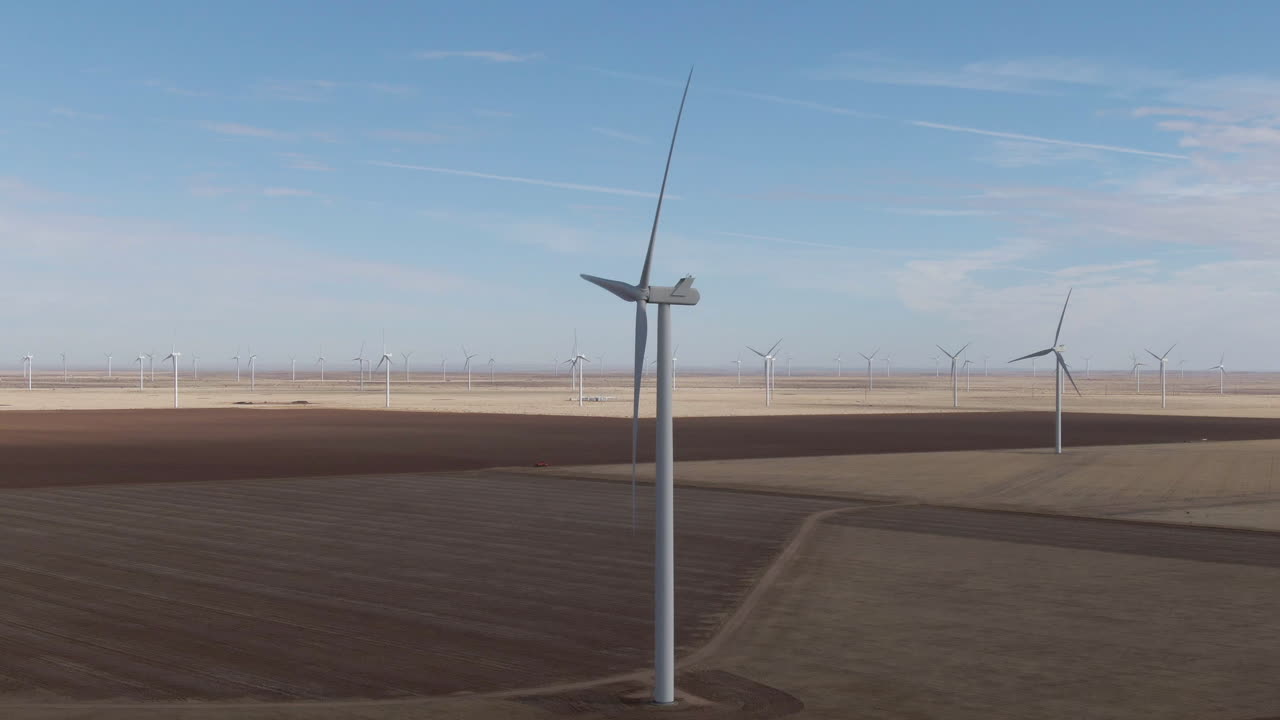 Aerial tracking shot of shadowy wind turbine amid a large wind farm in north Texas, USA