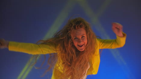 Funny-unusual-woman-with-long-hair-having-fun-smiling-dancing-in-studio-against-blue-background.-Music-dance-concept