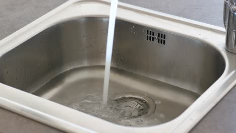 agua corriendo hacia un fregadero de cocina de acero inoxidable
