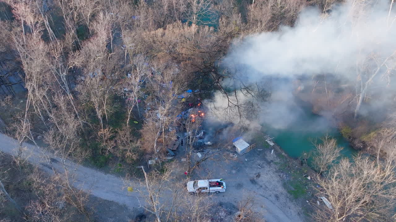 Aerial drone footage rotating around a homeless encampment that is on fire with lots of smoke.