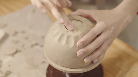 hands of female artisan smoothing bottom of handmade clay bowl