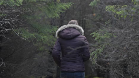 girl in a coat and hood walks alone in a forest in iceland