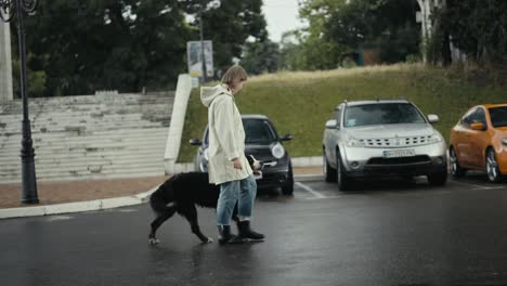 feliz mujer rubia en una chaqueta blanca camina por el parque con su gran perro después de la lluvia