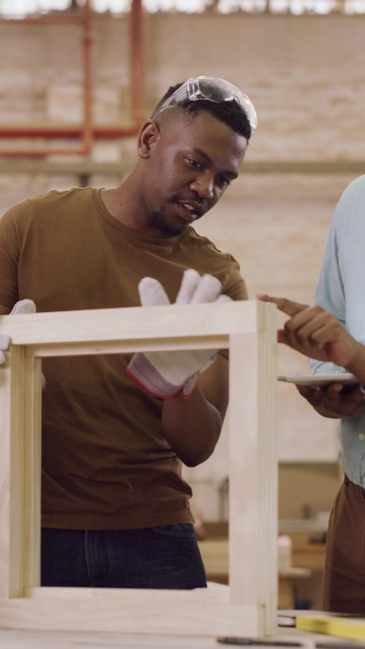 Two Men Discussing Wooden Frame Construction in a Workshop