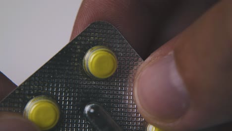 man-holds-blister-with-yellow-pills-on-light-background