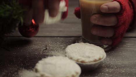 mano usando guantes de invierno agarrando pasteles y café en el fondo de navidad