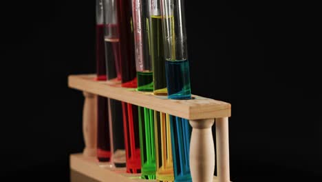 a wooden rack holds test tubes filled with colorful liquids against a dark background.