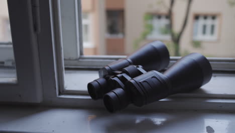 handheld shot of black binoculars placed on open white window, overcast day