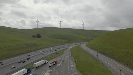 On-a-cloudy-day,-this-drone-footage-smoothly-pushes-into-the-tranquil-scene-of-Highway-580-meandering-through-the-verdant-Altamont-Pass,-its-rolling-hills-dotted-with-windmills-and-sparse-traffic