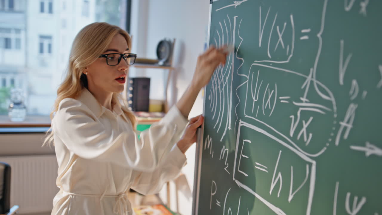 Teacher writing physic formulas on blackboard explaining information closeup