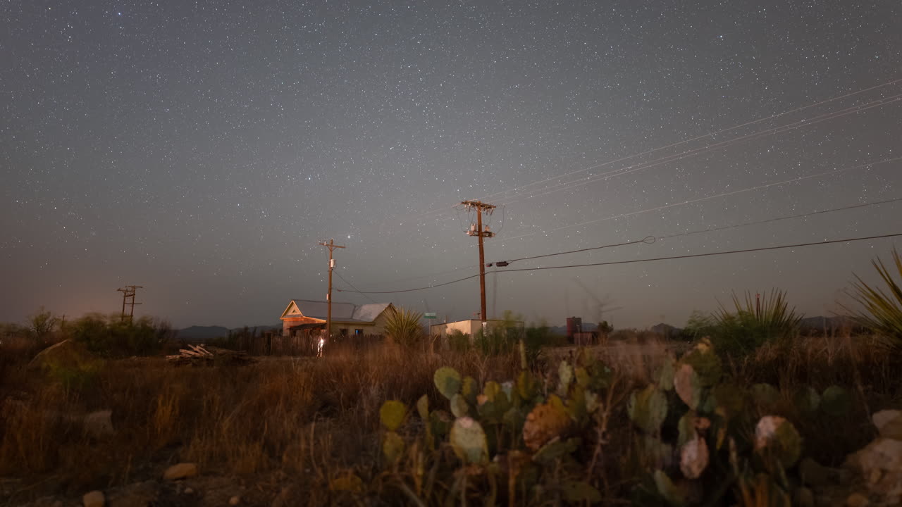 Stars and meteors rising over a west Texas landscape with telephone poles, cactus, and a small house
