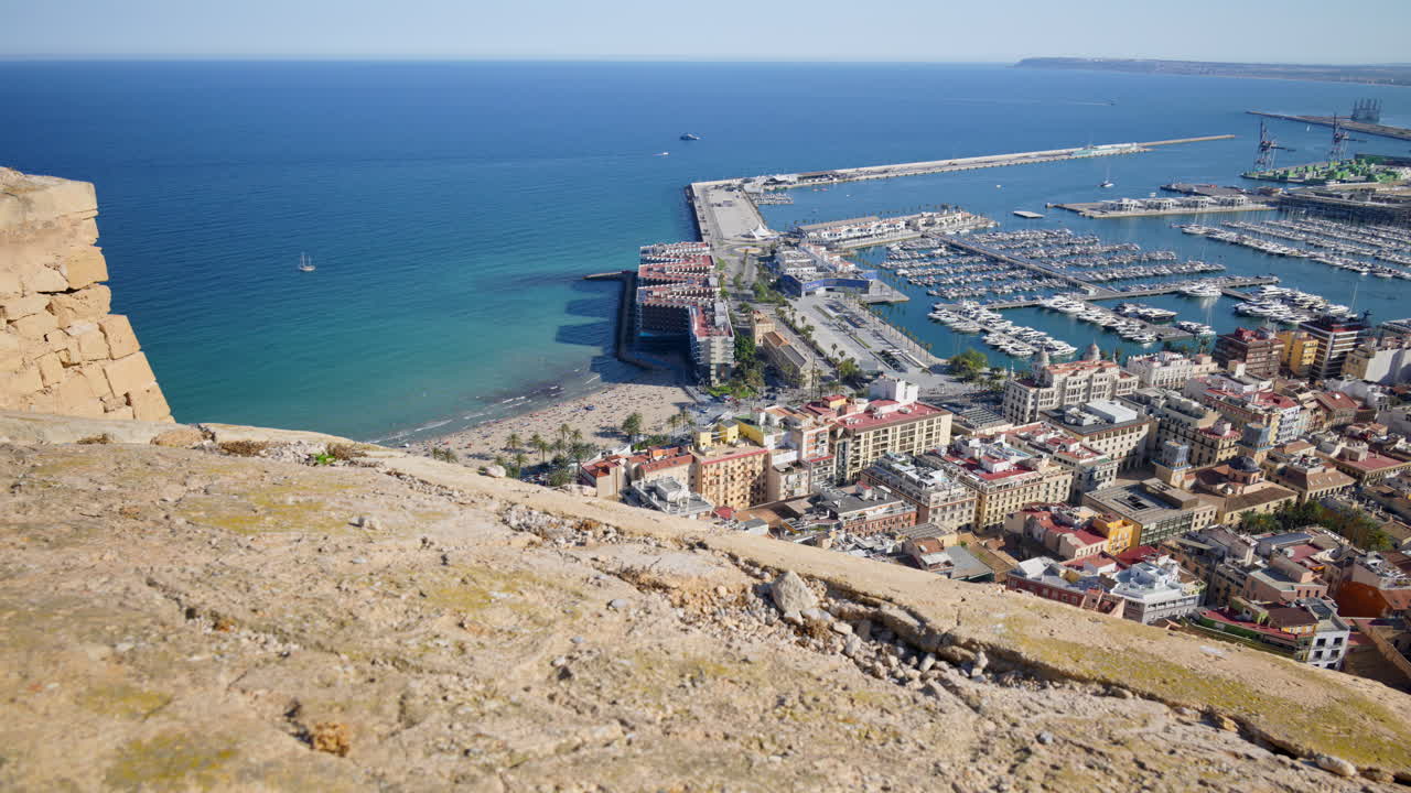 Sweeping view from the castle across Playa del Postiguet, the marina packed with yachts, and the long breakwaters of the Port of Alicante