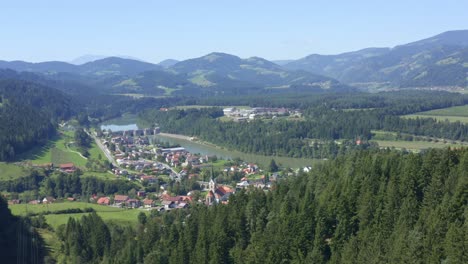 Aus-Der-Luft-Nähert-Man-Sich-Der-Charmanten-Stadt-Am-Fluss,-Umgeben-Von-Wäldern-Und-Bergen