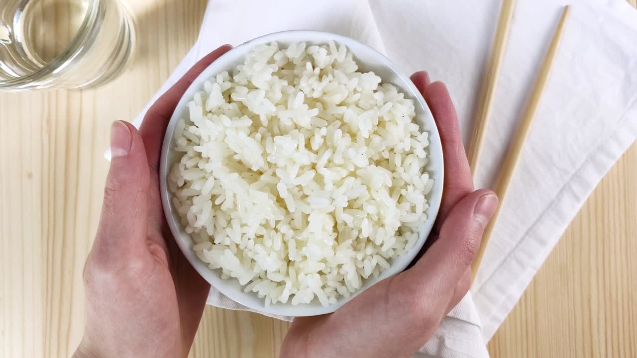 arroz blanco hervido en un cuenco redondo. las manos femeninas sostienen el plato