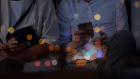 Flecken-Von-Bokeh-Lichtern-Vor-Dem-Mittelteil-Eines-Mannes-Und-Einer-Frau,-Die-Ihr-Smartphone-Benutzen