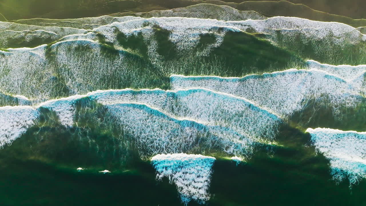 Amazing beautiful waves moving the sandy beach of Morro Bay, California, USA. White foamy tide slowly moving to the shore. Bird's eye view.