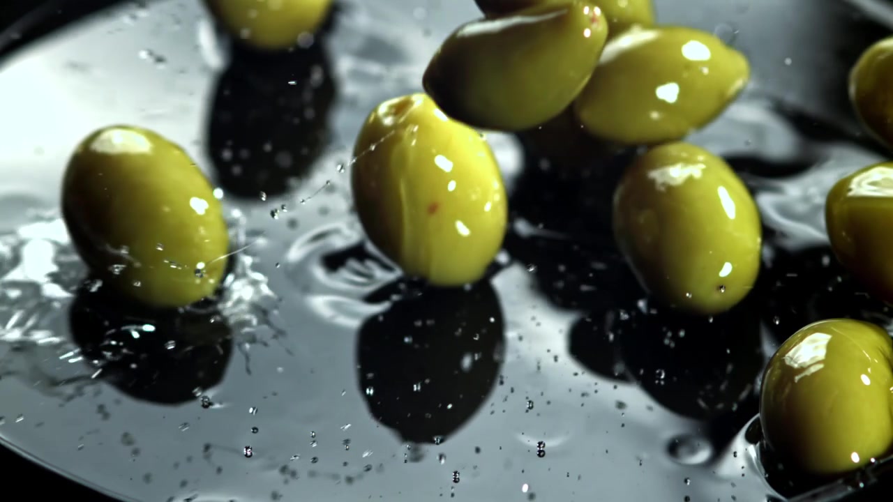 Olive verdi fresche che schizzano su una superficie scura e bagnata