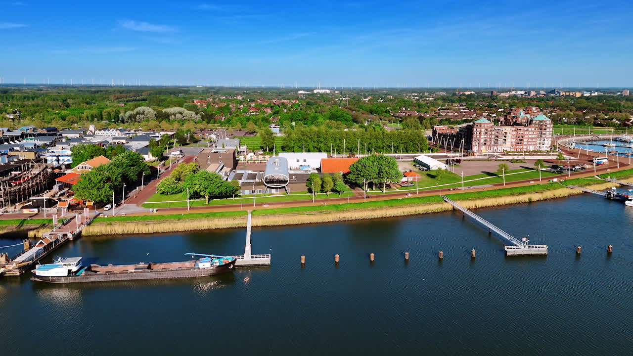 Flying closer to the bright sunny lakefront of Lelystad, the Netherlands. View on the historical museum and green scenery of the city.