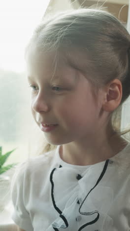 happy little girl turns head standing at small blackboard in home classroom closeup. cute cheerful schoolgirl tries to find answer at lesson