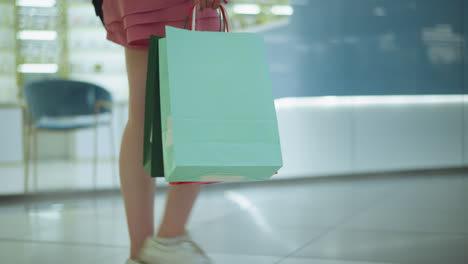 vista de la pierna de la dama llevando bolsas de compras coloridas mientras camina a través de un centro comercial brillantemente iluminado, un ligero borrón de artículos de la tienda visibles en el fondo mientras se mueve majestuosamente a través del piso