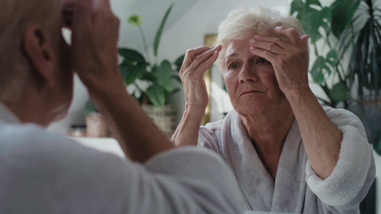 Senior woman checking skin condition in the bathroom mirror