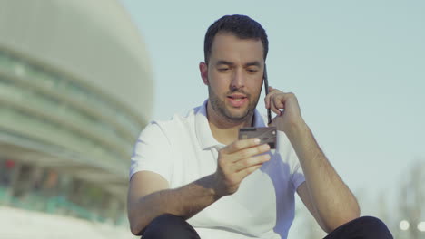 Focused-man-holding-credit-card-and-dictating-bank-account-details.