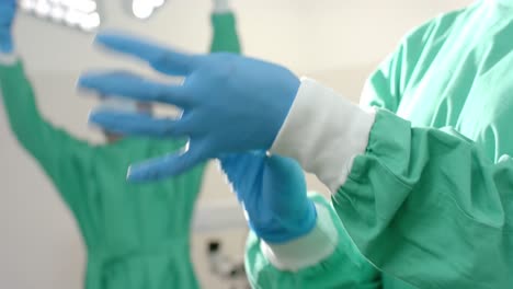 midsection of caucasian female surgeon wearing medical gloves in operating theatre, slow motion