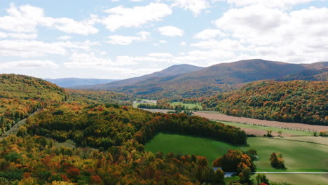 Aerial-drone-shot-over-beautiful-Vermont-mountains-during-peak-fall-foliage-with-quaint-town-in-distance