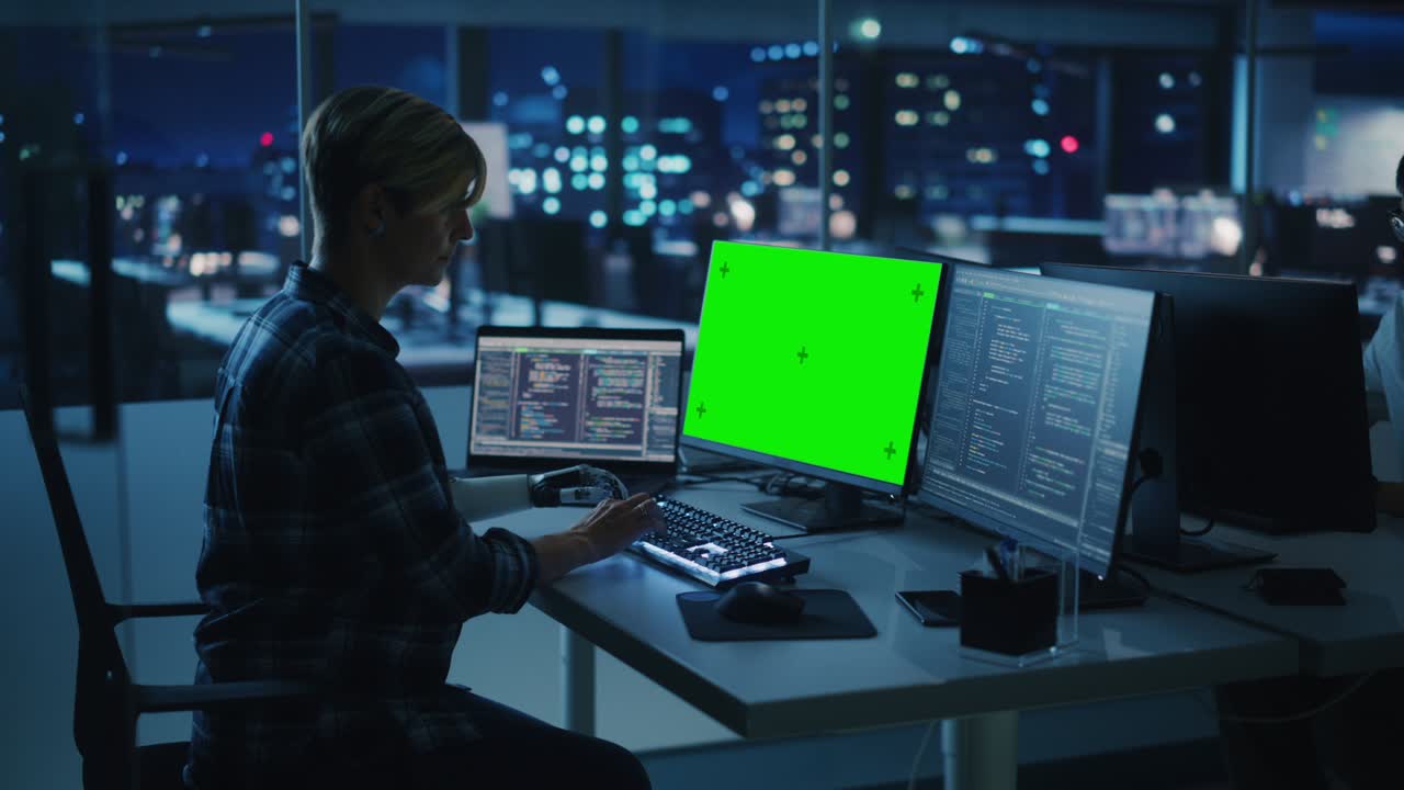 trabajo en equipo diverso en la oficina por la noche: persona con discapacidad que utiliza un brazo protésico para trabajar en una computadora de pantalla verde. equipo de ingenieros de software trabaja hasta tarde para crear una aplicación innovadora