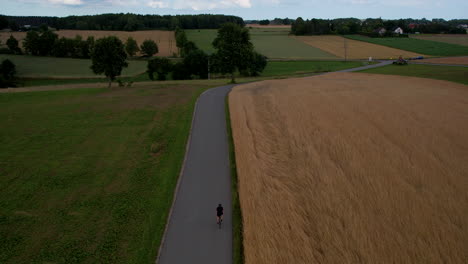 Cyclist-riding-towards-highway-with-cars-in-a-rural-scenic-place